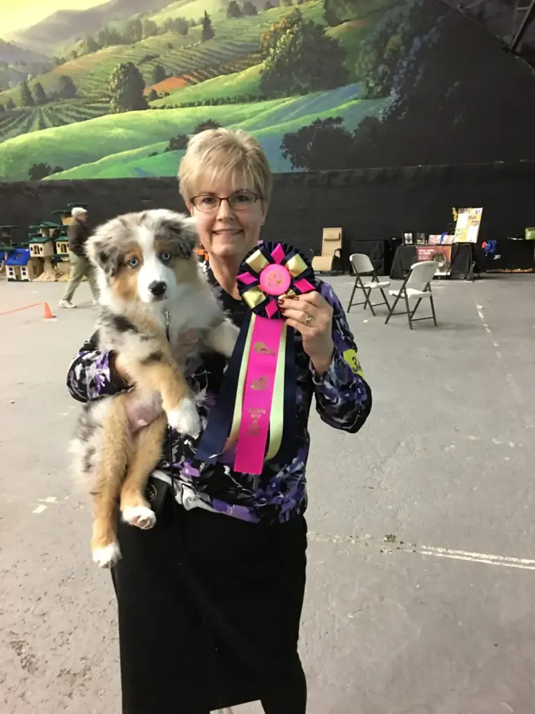 Lori holding young Bowie and his pink rosette at a dog show