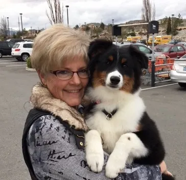 Lori McClelland hugging Ivy as a five-month-old black tri puppy